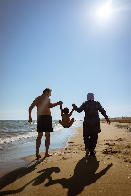 Muslim family, dad and mom with burkini on the beach walking near sea