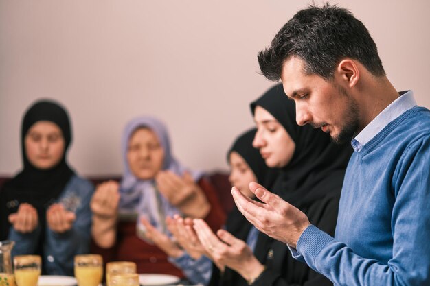 Muslim family making iftar dua to break fasting during Ramadan at home together pray with hands up