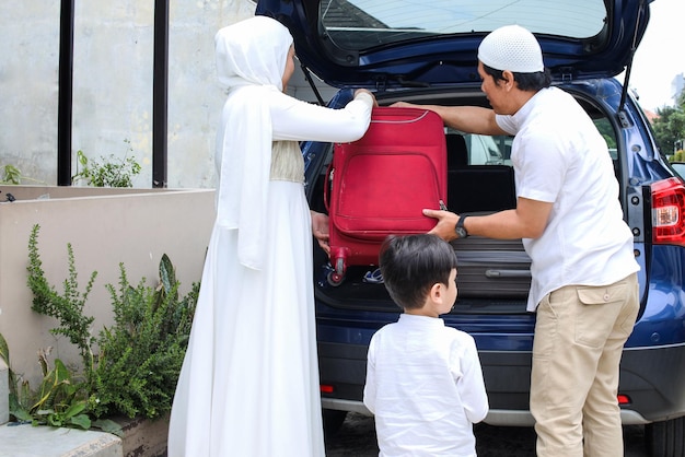 Muslim family moving the suitcases into the trunk of the car ready to go on mudik during eid