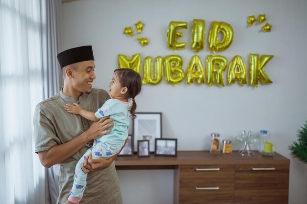 Muslim father and kid cuddling with eid mubarak decoration