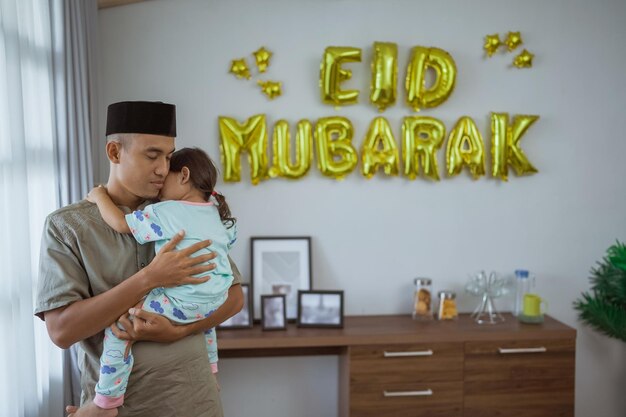 Muslim father and kid cuddling with eid mubarak decoration