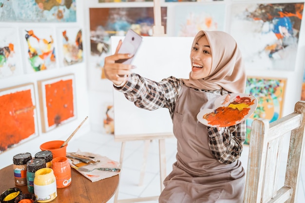 Foto artista femminile musulmana che scatta foto di selfie con il proprio dipinto