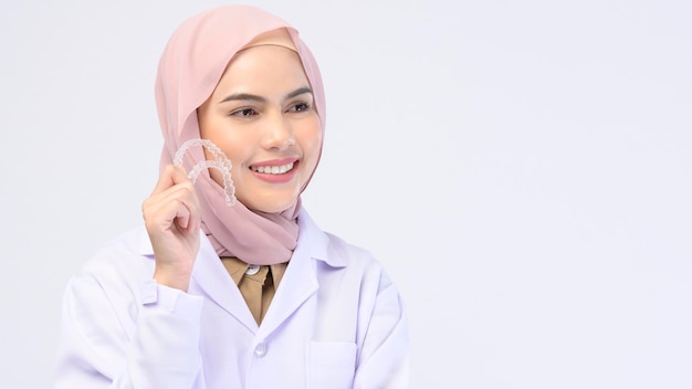 A muslim female dentist holding invisalign braces over white background studio