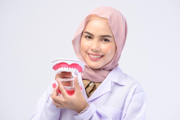 A muslim female dentist holding Invisalign braces over white background