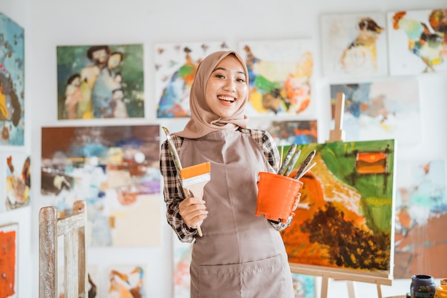 Muslim female painter holding brush and bucket smiling