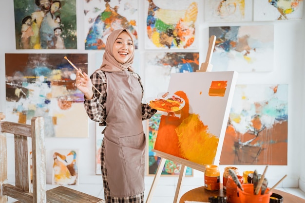 그녀의 작업장에서 캔버스에 그림을 그리는 이슬람 여성 화가