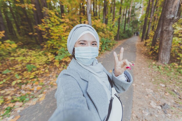 Muslim girl in a medical mask makes a selfie portrait of islamic arabian female student in park