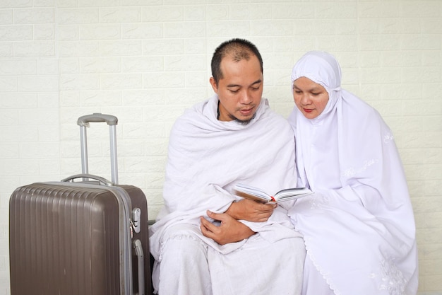 Мусульманская пара хаджа в белых одеждах вместе молится с Аль-Кораном