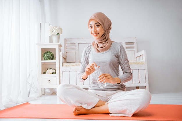 Muslim hijab woman smile and drinking from bottle after exercise yoga home workout on orange matress