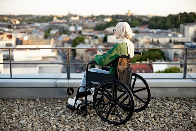 Photo muslim lady with phone taking in view of city in wheelchair