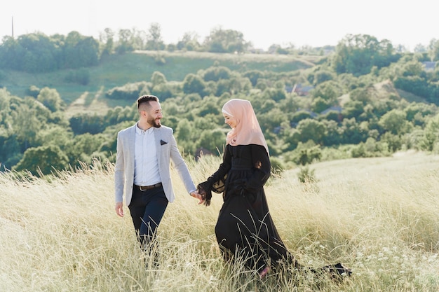 Muslim love story of mixed couple. Man and woman smiles and walks on the green hills