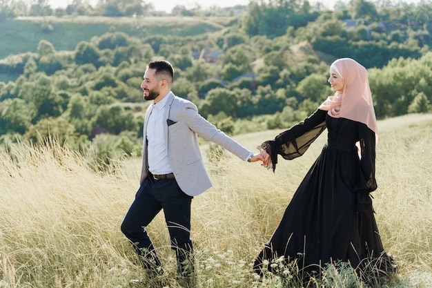 사진 혼합 커플의 이슬람 사랑 이야기. 남자와 여자는 미소를 짓고 푸른 언덕을 걷는다.