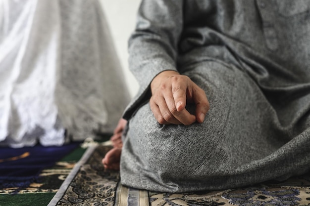 Muslim man praying, sitting in tahiyat position with index finger raised, close-up.