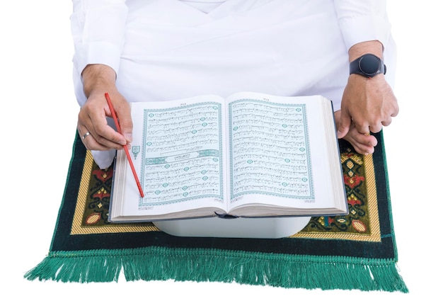 A Muslim man sitting and reading the Quran on the prayer rug