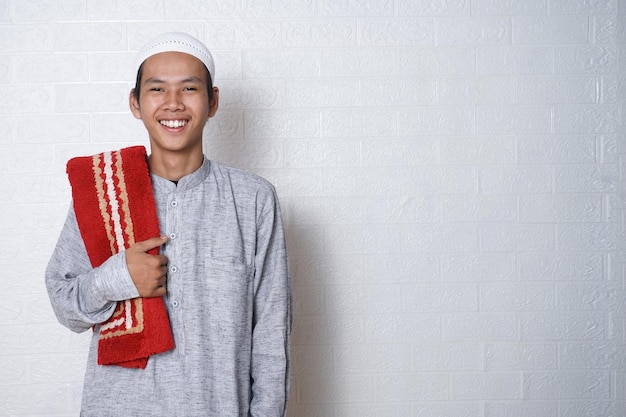 Foto un uomo musulmano, sorridente, indossa un cappello e un tappeto da preghiera.