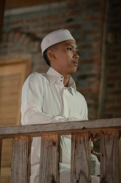 A Muslim man standing on the balcony of a wooden house in the village