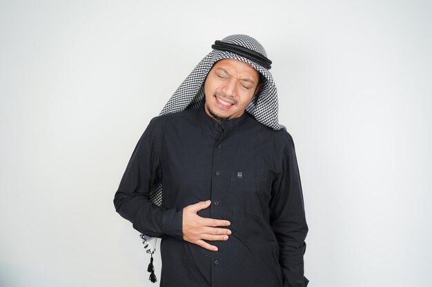Muslim man wearing Arab turban sorban having stomach ache bending over holding hands