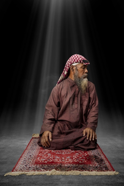 Muslim man with a beard wearing keffiyeh with agal in praying position salat on the prayer rug