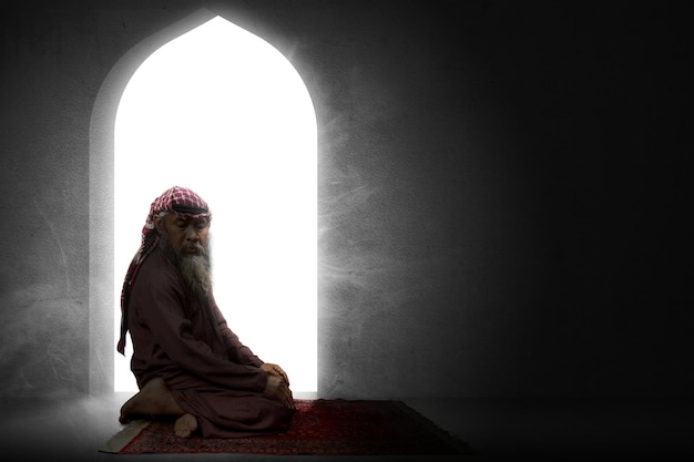 Muslim man with a beard wearing keffiyeh with agal in praying position salat on the prayer rug