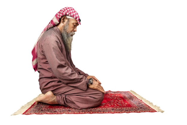 Muslim man with a beard wearing keffiyeh with agal in praying position salat on the prayer rug