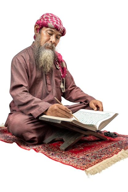 Muslim man with a beard wearing keffiyeh with agal sitting and reading the Quran on the prayer rug