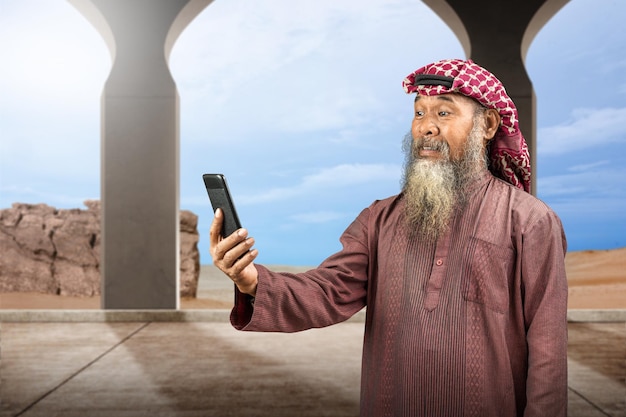 Muslim man with a beard wearing keffiyeh with agal using mobile phone