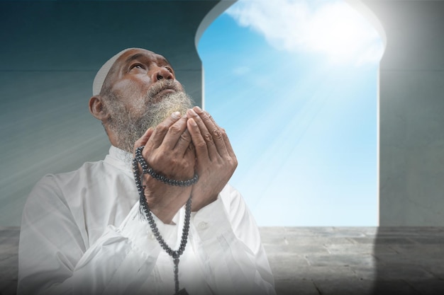 Muslim man with a beard wearing a white cap praying with prayer beads on his hands