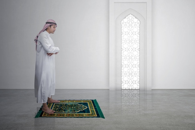 Мусульманин с куфией с агалом в молитвенной позе на молитвенном коврике