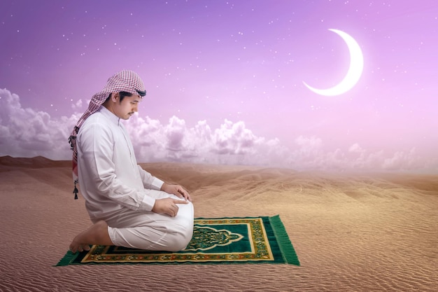 Muslim man with keffiyeh with agal in praying position salat on the prayer rug