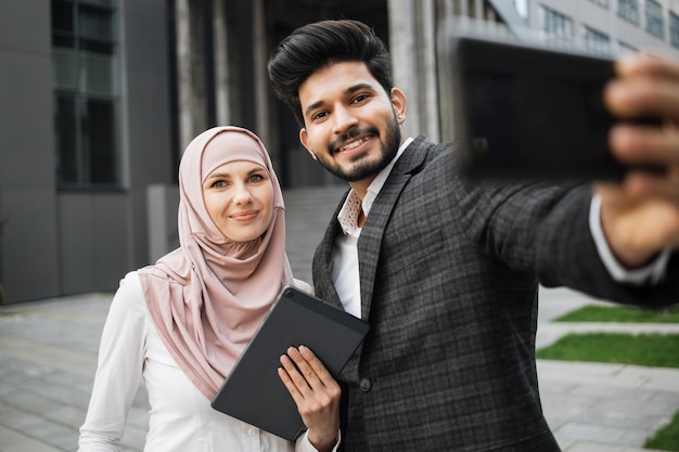 イスラム教徒の男性と女性が携帯電話で自分撮りをしている正式な服装をしている