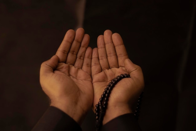 Photo muslim men raise their hands to pray with a tasbeeh on dark background indoors focus on hands