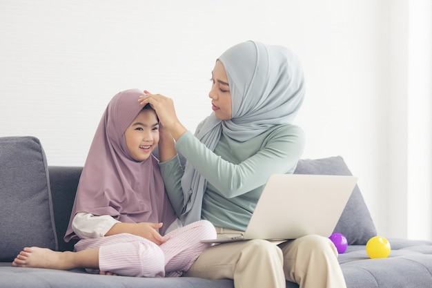 La mamma musulmana in hijab è la sua piccola figlia con il computer seduta in soggiorno. relazione amorosa