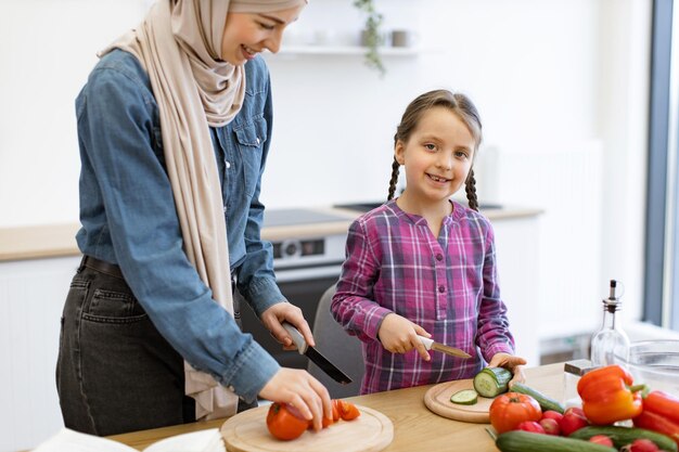 Muslim mother and daughter cutting ingredients for salad in kitchen
