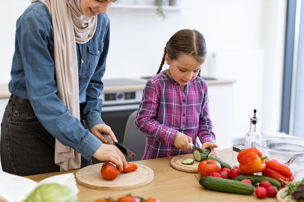 Muslim mother and daughter cutting ingredients for salad in kitchen