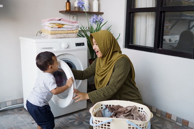 Muslim mother a housewife with a baby engaged in laundry with washing machine