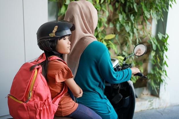 Madre musulmana che porta la figlia a scuola in moto al mattino. studente delle elementari asiatico torna a scuola