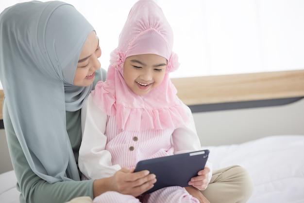 태블릿 및 집에서 귀여운 작은 아기와 함께 일하는 이슬람 어머니.