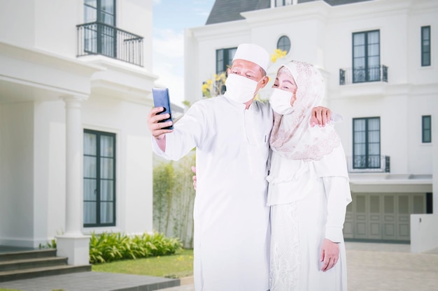 Muslim old couple takes selfie in front of house