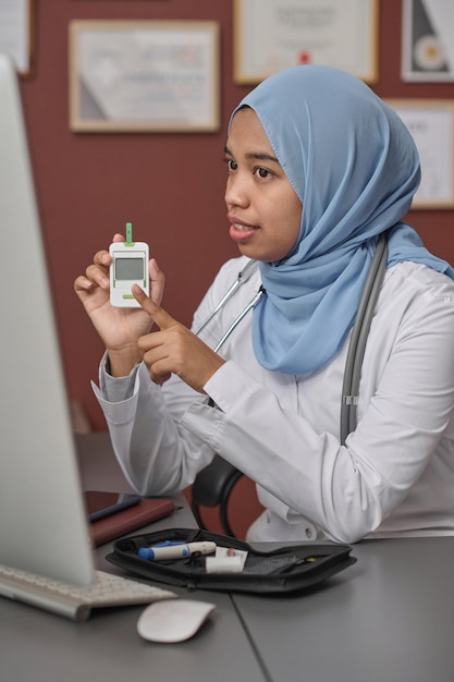 Photo muslim physician showing glucometer to patient at online appointment