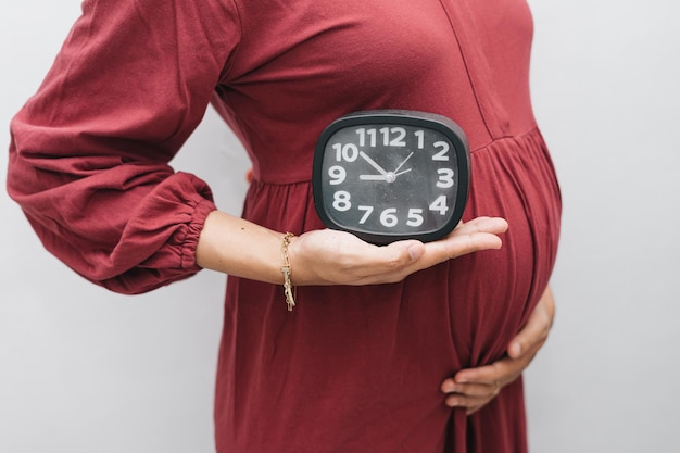 Photo muslim pregnant woman holding her belly stomach and clock watch