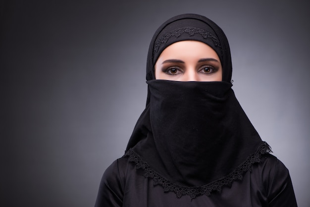 Muslim woman in black dress against dark background