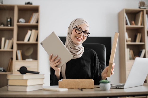 Muslim woman doing live stream while unpacking box with new tablet