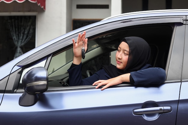 Muslim woman in hijab driving and showing car keys out the window.