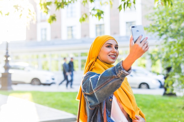 Muslim woman in hijab makes a selfie on the phone standing on the street of the city