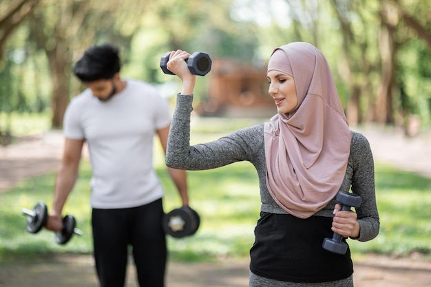 Muslim woman and man exercising with dumbbells at park