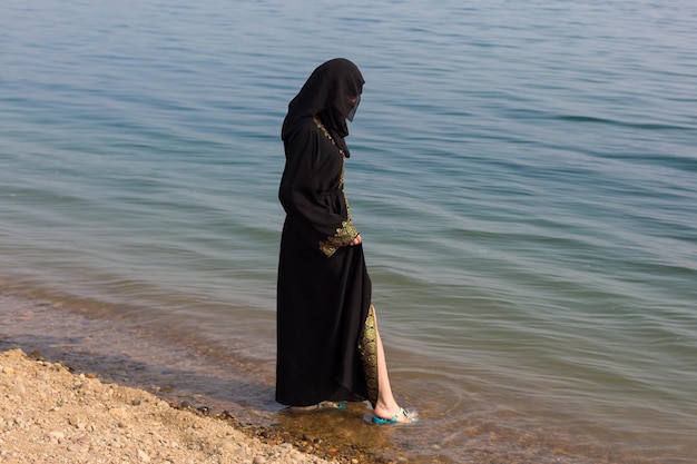 A Muslim woman in national clothes wets her feet in the sea