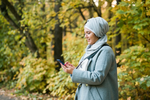 스마트폰을 사용하여 공원에서 온라인 무선으로 연결된 이슬람 여성. 광고를 위한 공간