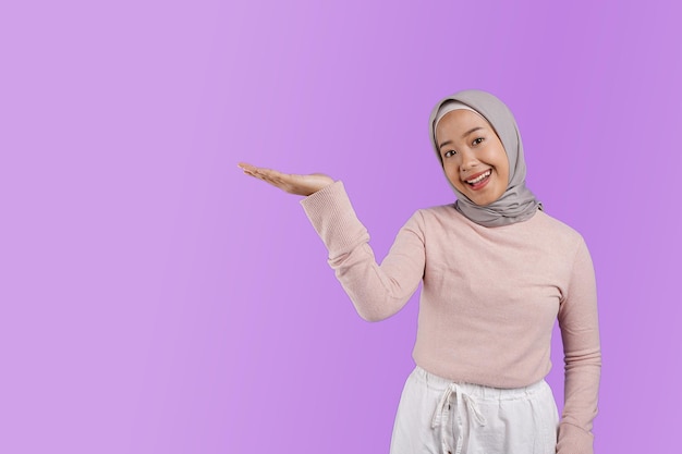 A muslim woman in a pink hijab is smiling and is holding her hand up to the sky