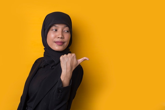 Muslim woman pointing her finger at something on a yellow background