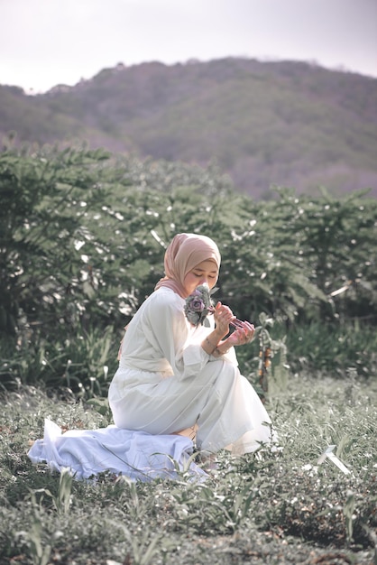 Muslim Woman Sitting at the Garden holding flower in a Sunny Day